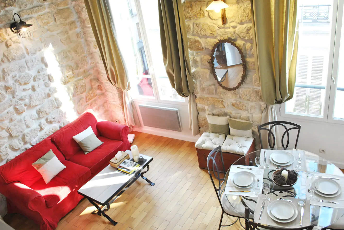 View of a living room with a red couch next to a glass table and chairs.