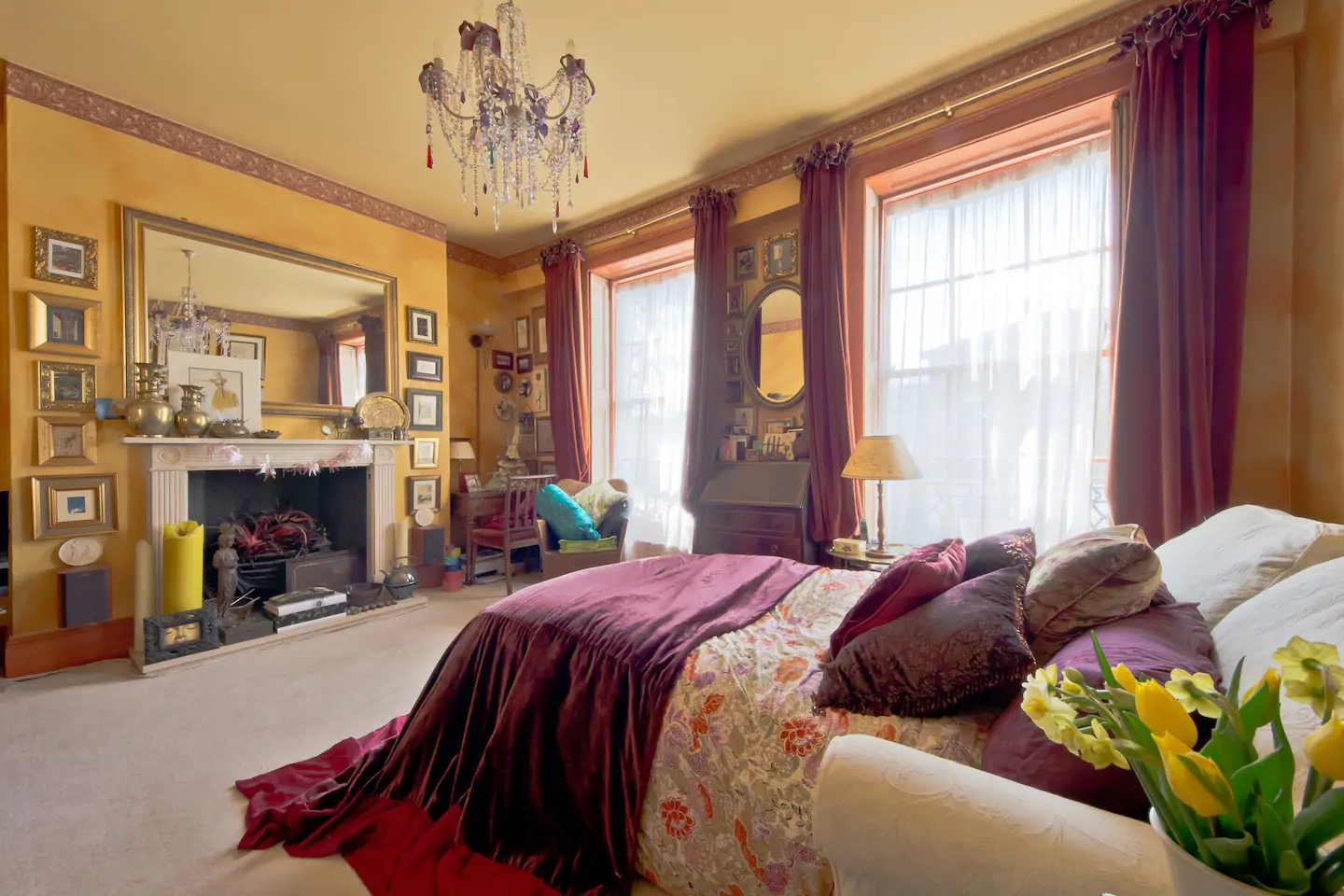 Elegant bedroom with a maroon and gold bed and chandelier hanging from the ceiling.