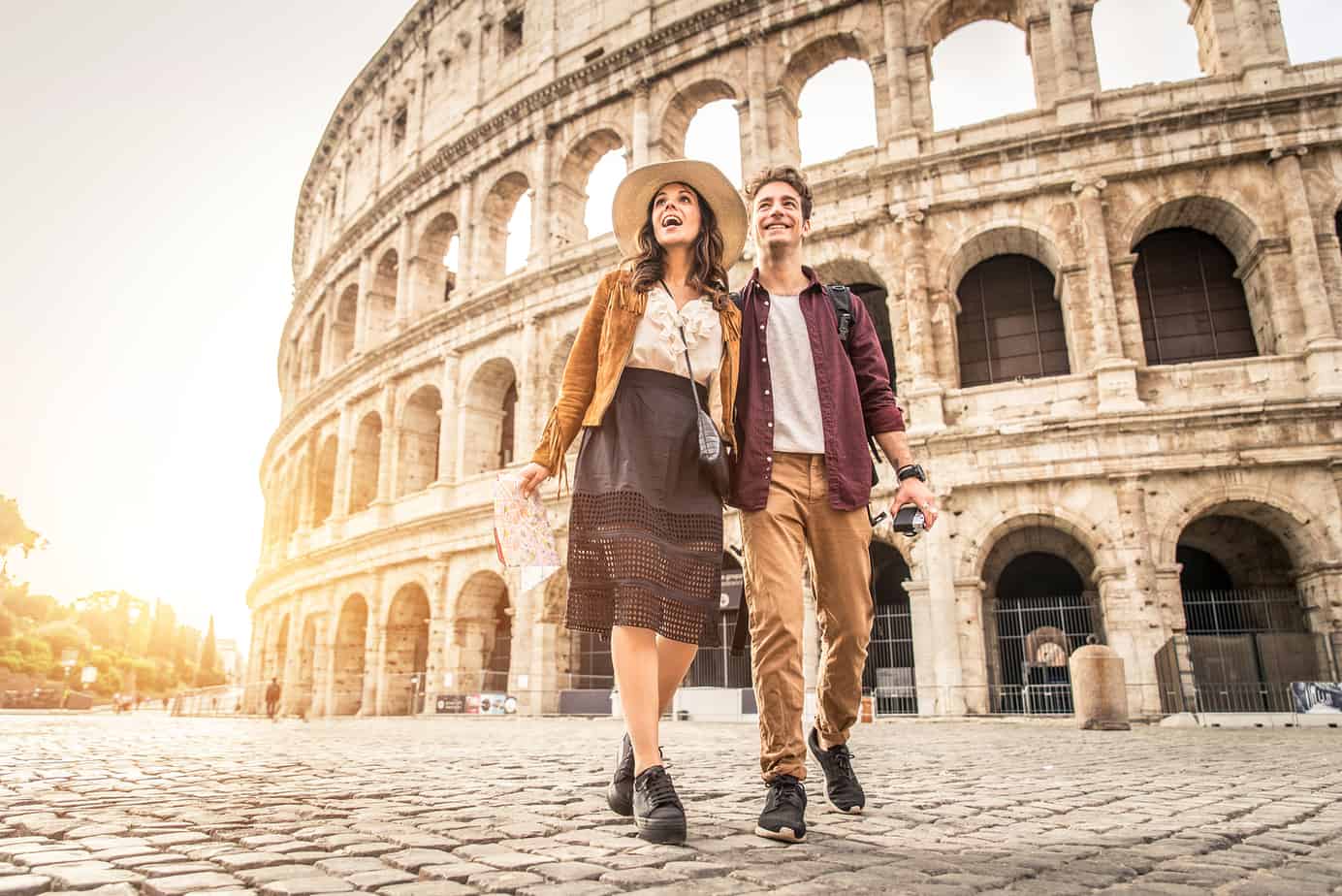 A couple walks while smiling in front of the Coloseum.