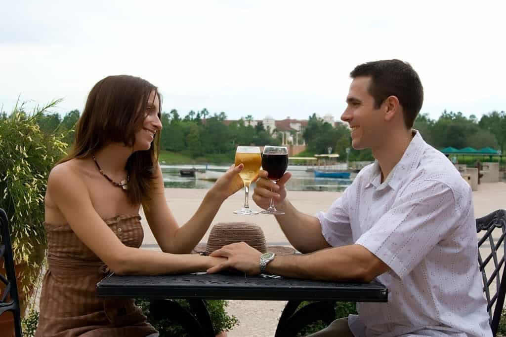 A couple sits outdoors at a restaurant while clinking wine glasses.