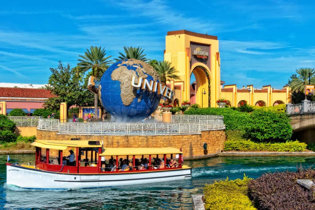 People ride by in a red boat on water next to a world globe that says Universal.