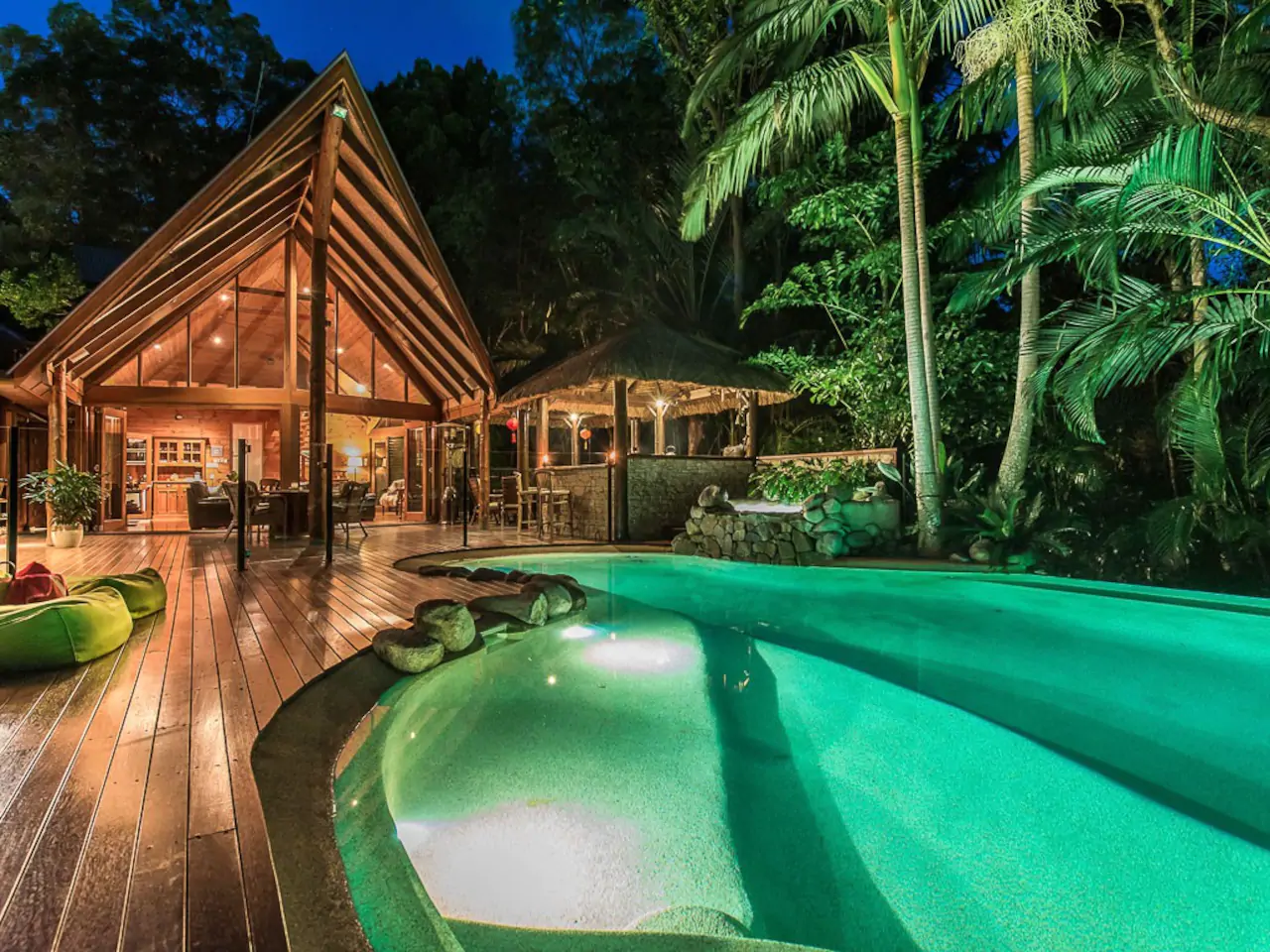 A big blue pool is situated outdoors on a wooden deck. A big cabin is behind.