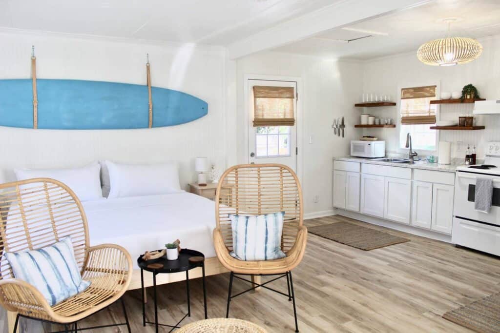 A studio apartment has a blue surfboard on the wall, kitchen area on the right wall, and a bed.