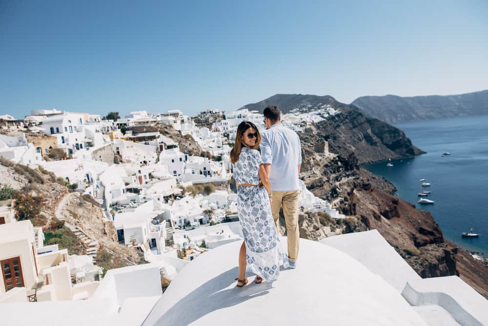 A couple stands on a rooftop in Greece. The woman looks back at the camera.