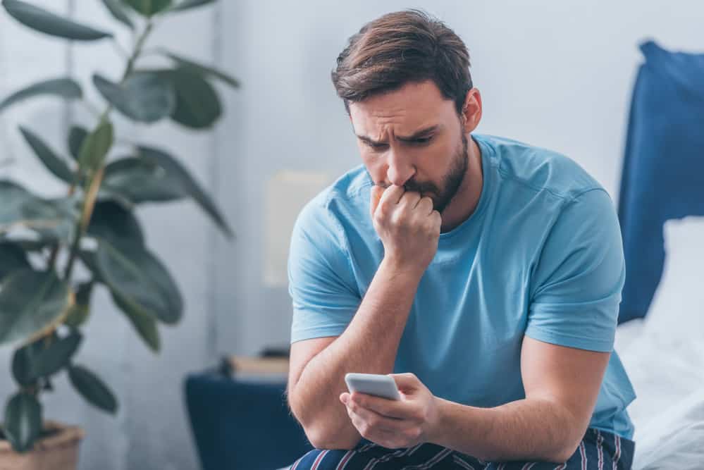 A man looks stressed while looking on his phone.