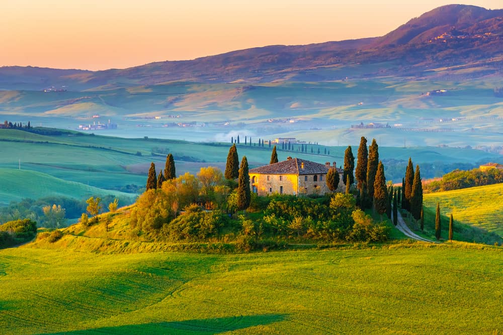 Classic Italian home surrounded by trees with hills in the distance.