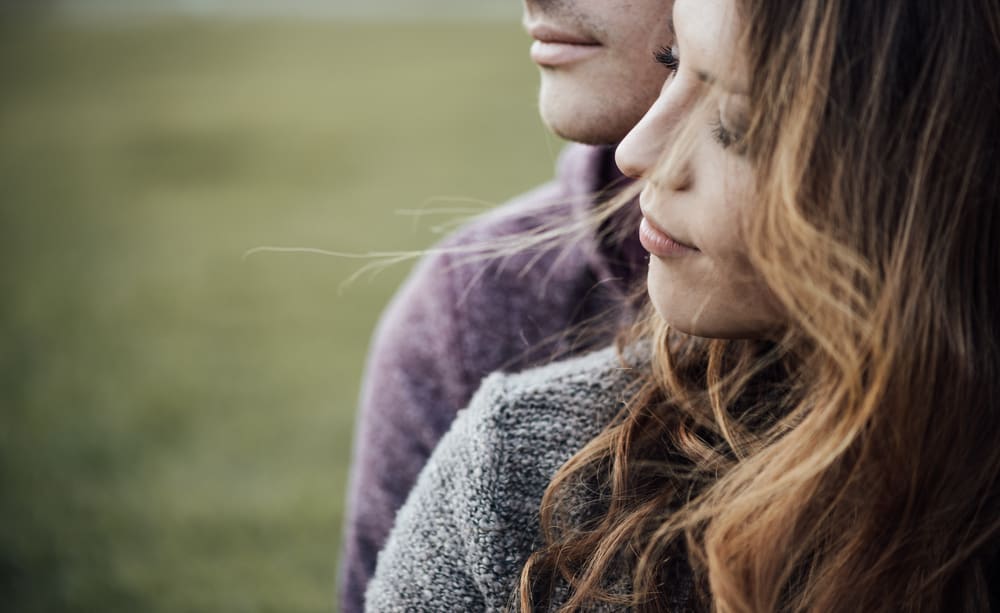 A man holds a woman from behind outdoors.