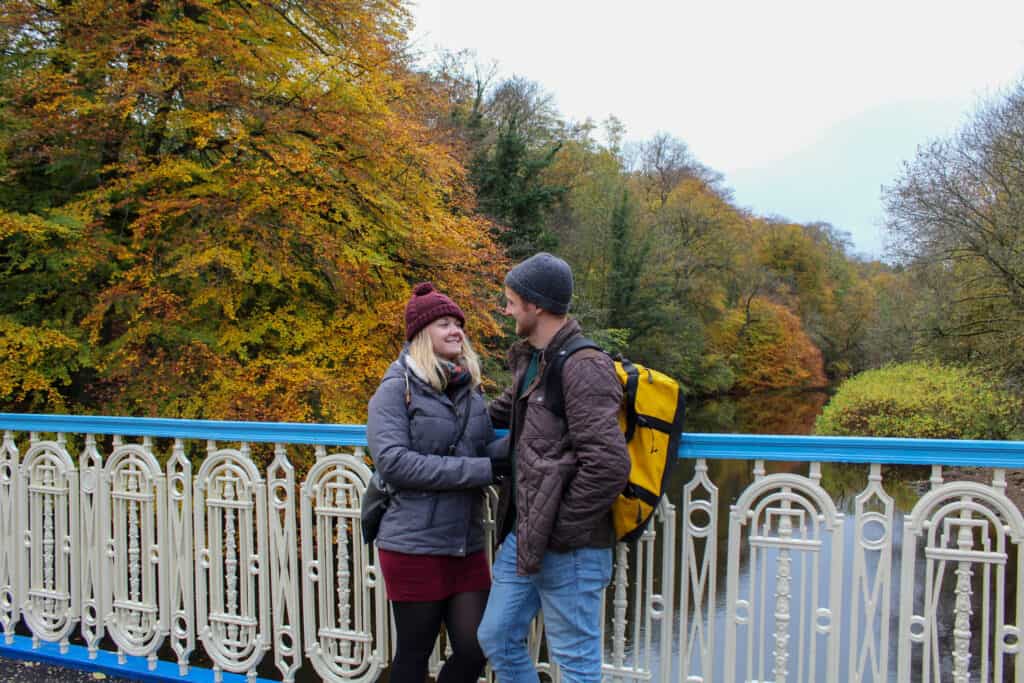 A couple smiles at each other on a bridge in the fall.