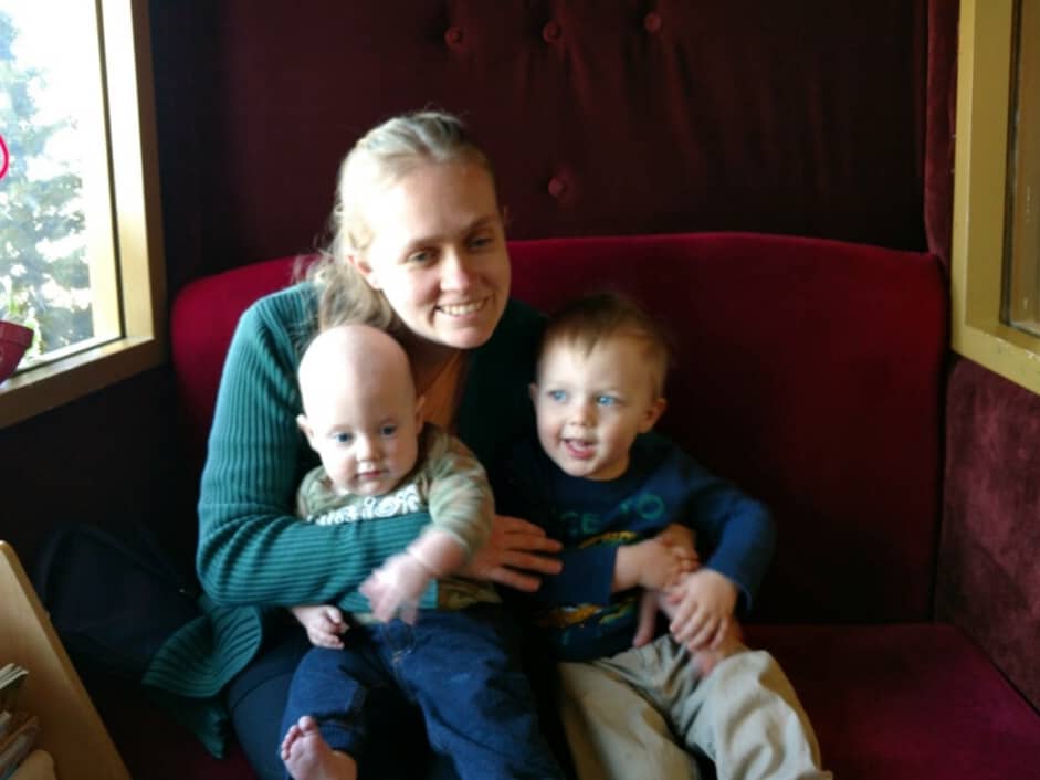 A woman holds two children on a red couch.