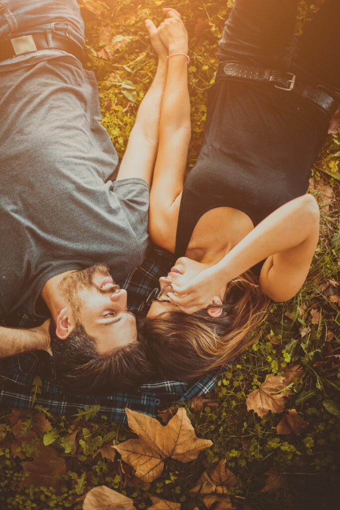 A couple lays together outside surrounded by fall leaves.