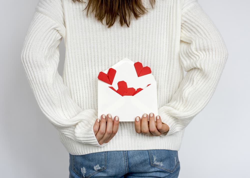 Woman holding an envelope filled with hearts behind her back.