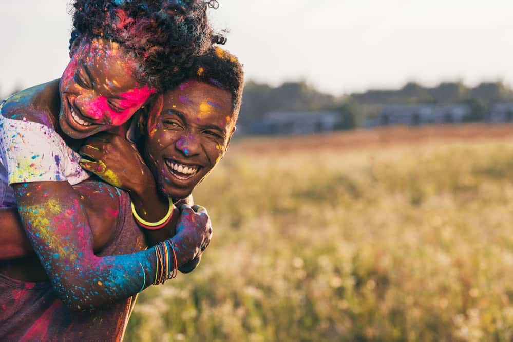 A couple is smiling and embracing each other in a field while covered in color.
