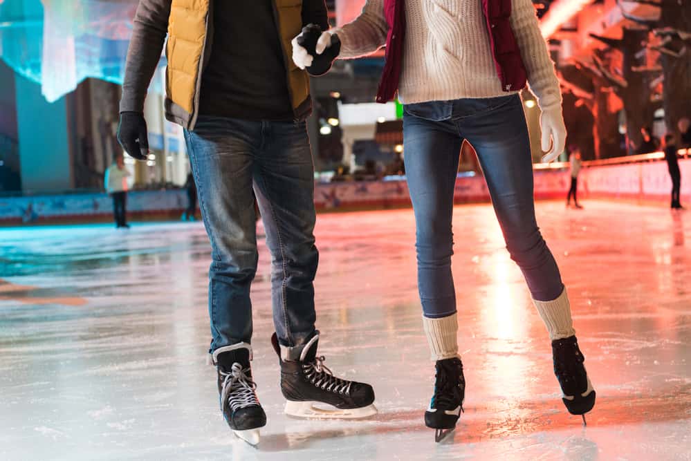 A couple ice skates on a rink with colored lights behind them. 