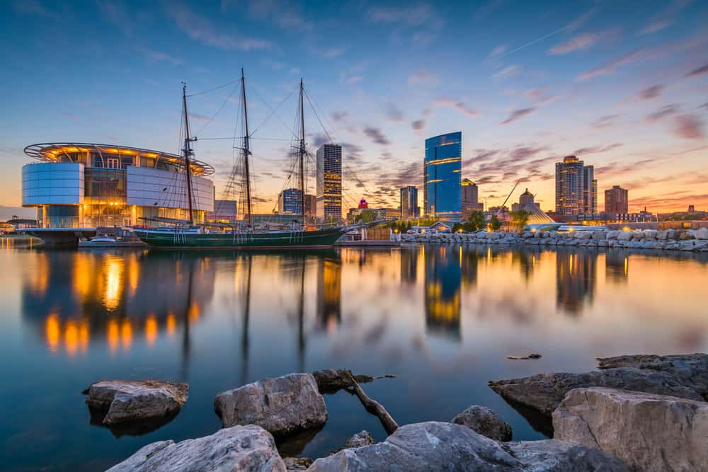 A calm body of water at sunset. Boats float on the water and skyscrapers are on the other side of the water.