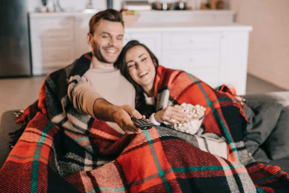 A couple is cozy and snuggled in together while eating popcorn and watching a show