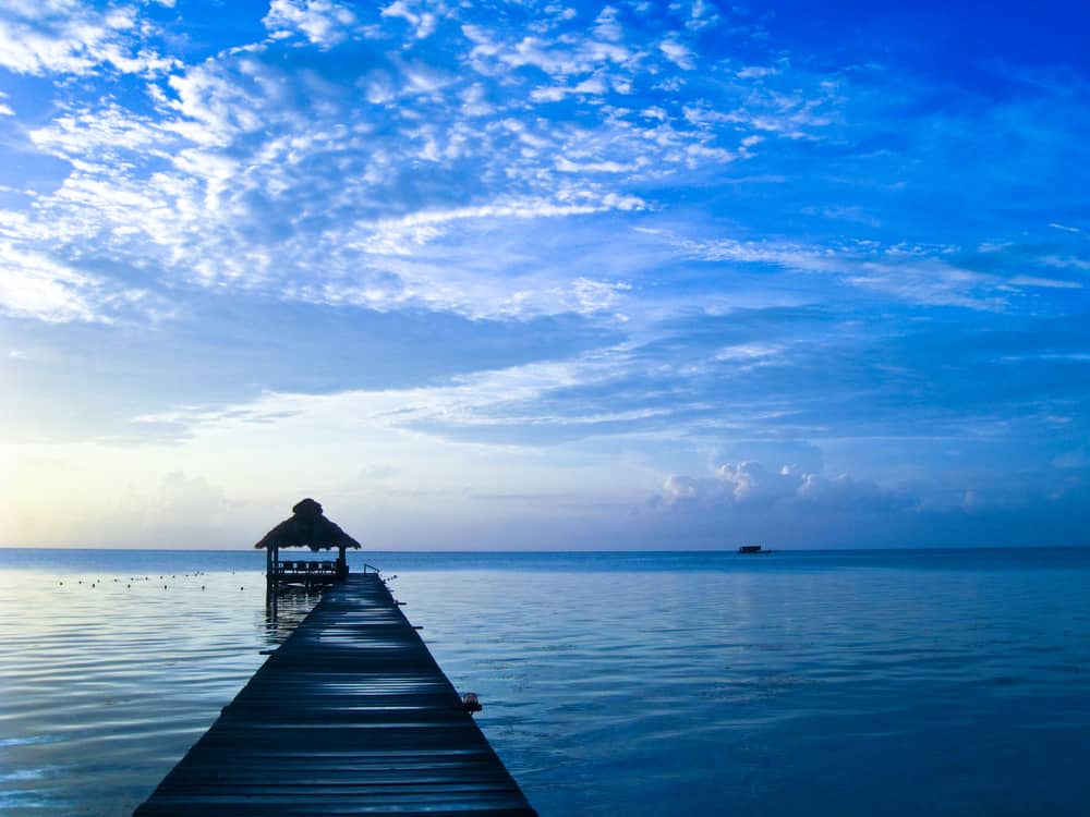 Wooden pier leads out to the ocean under a blue cloudy sky.