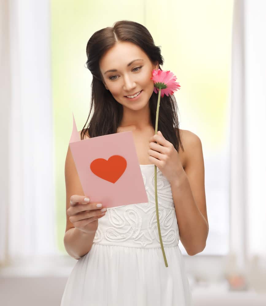 A woman reads a pink card while holding a pink flower.