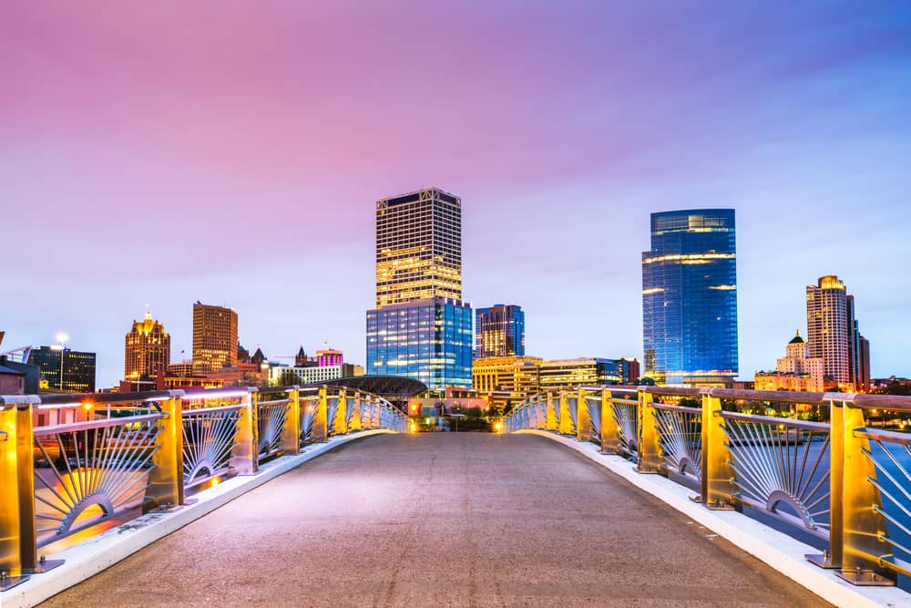 A walkway leads towards a city skyline under a pink and purple sky.