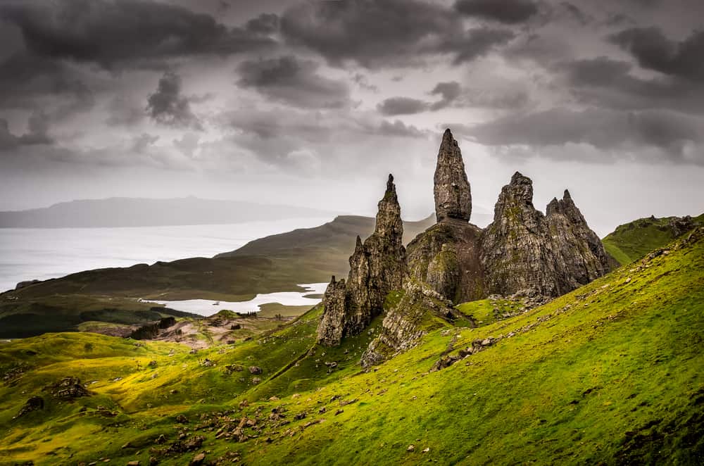 Large, rocky formations on the side of a grassy hill with dark grey clouds above. 