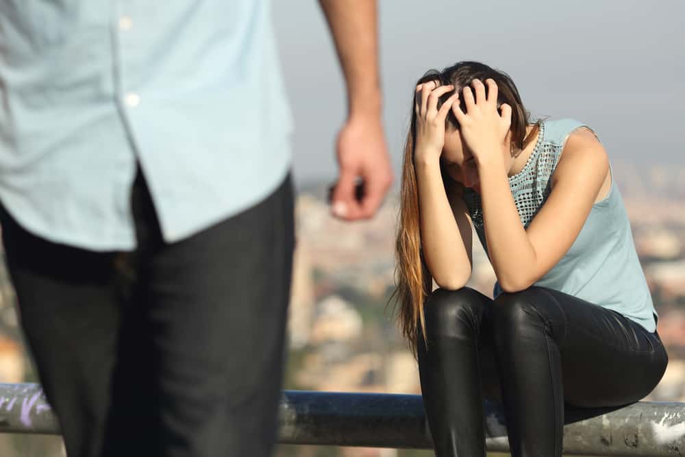 header image warning signs of a toxic relationship - man walking away from woman who is sitting with her head in her hands