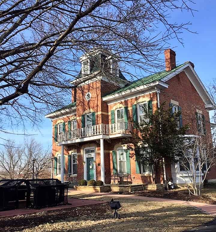 A brick building with green trim surrounded by trees.