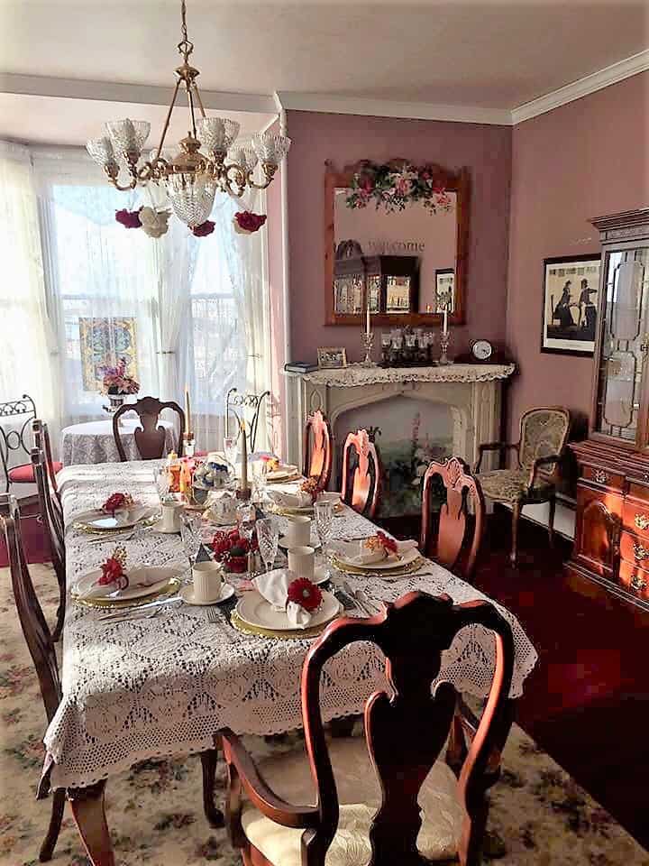 A table and chairs is set with a lace tablecloth. A chandelier hangs over the top.