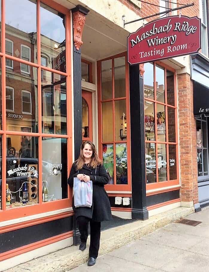 A woman smiles holding a bag in front of a winery storefront.