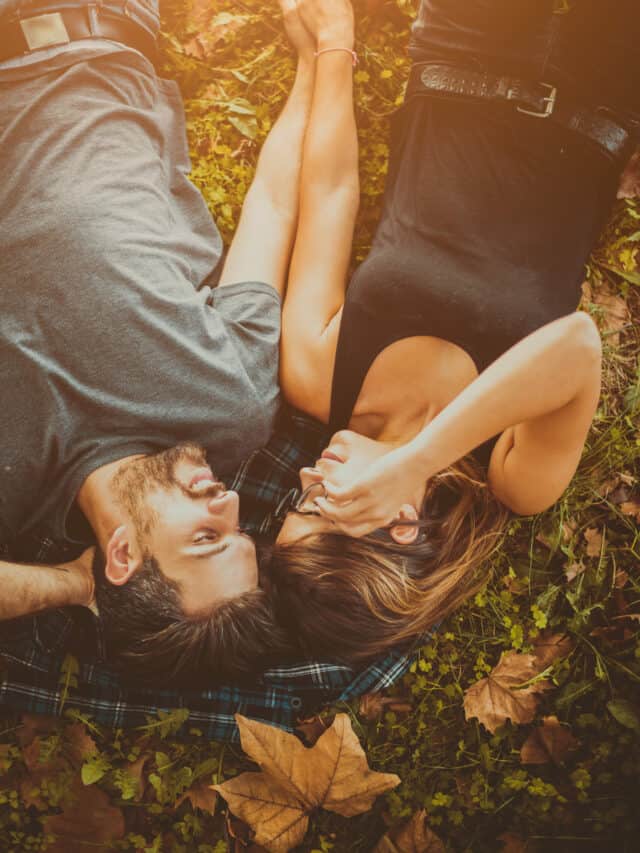 A couple lays together outside surrounded by fall leaves.
