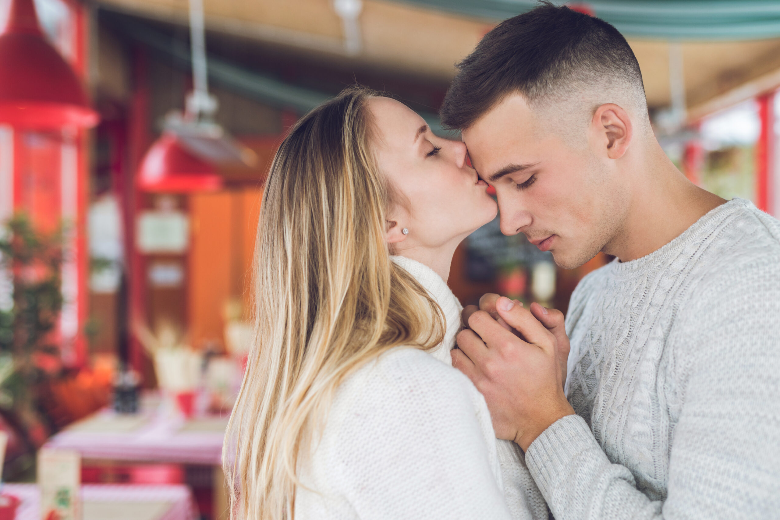 A woman kisses the forehead of her boyfriend inside a restaurant.