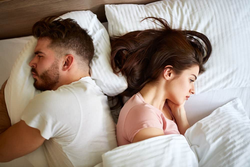 Young couple in quarrel in bed - man and woman laying down facing away from one another