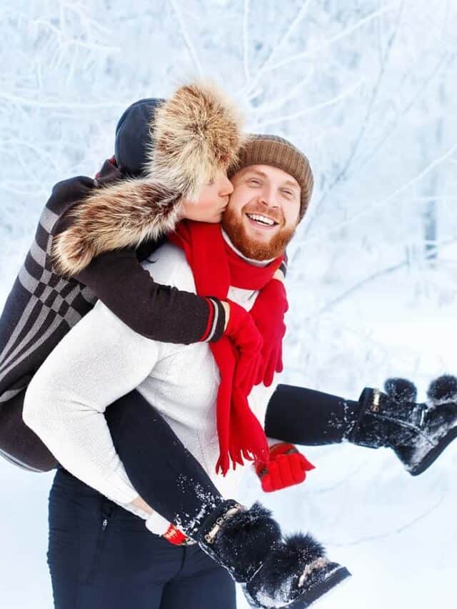 A man gives a woman a piggyback ride on a winter day surrounded by trees.
