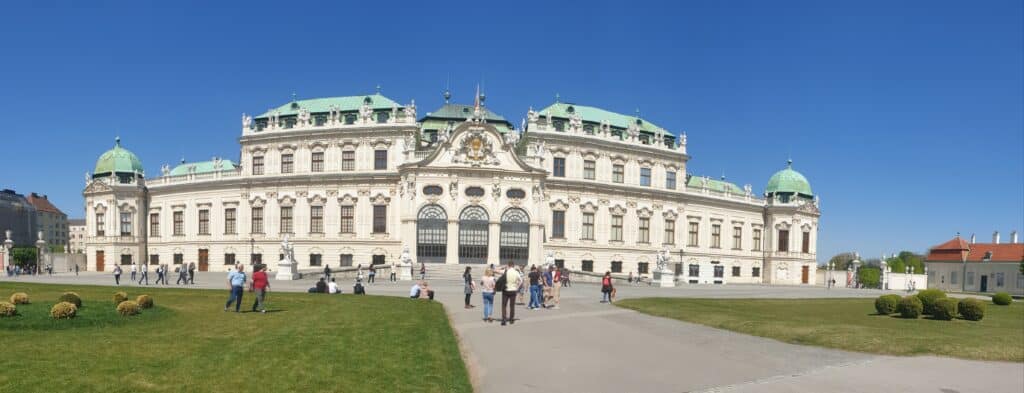 People walk around in front of a palace.