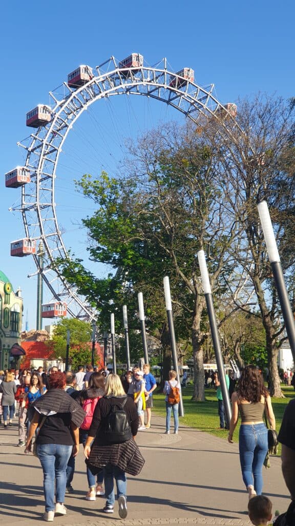 People walk around with a ferris wheel behind them.