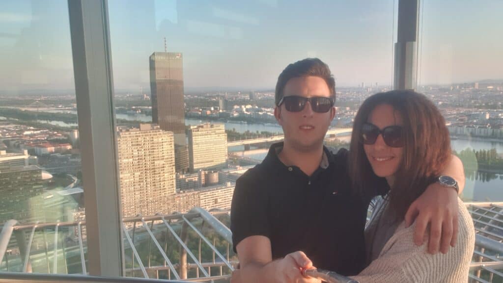 A couple smiles with a view of a city behind them.