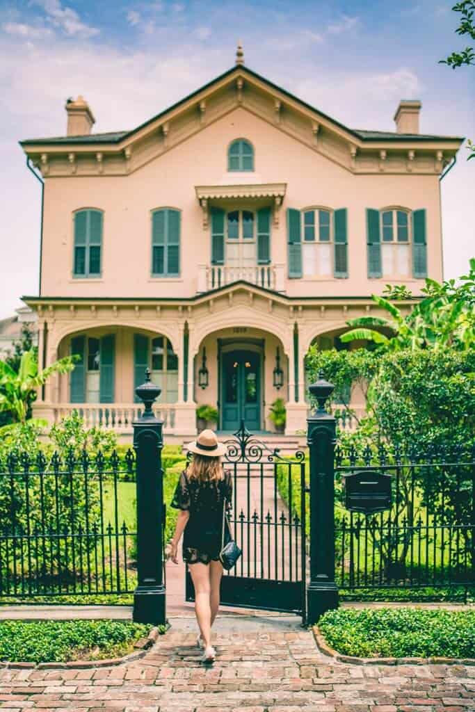 A woman walks through wrought iron gates leading to an old Southern house.