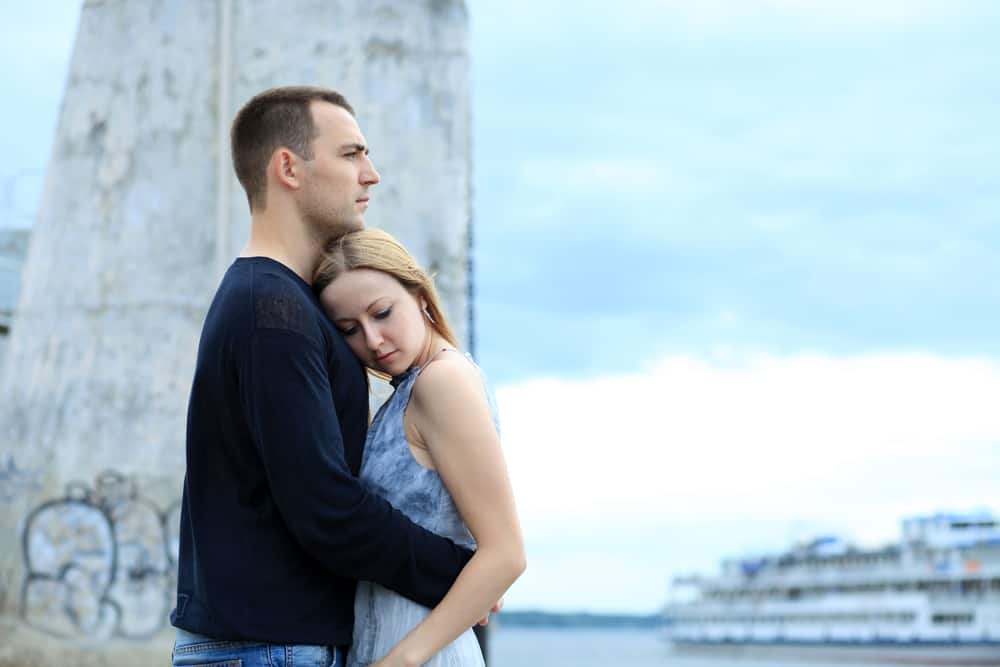 A man hugs a woman with the water behind them.