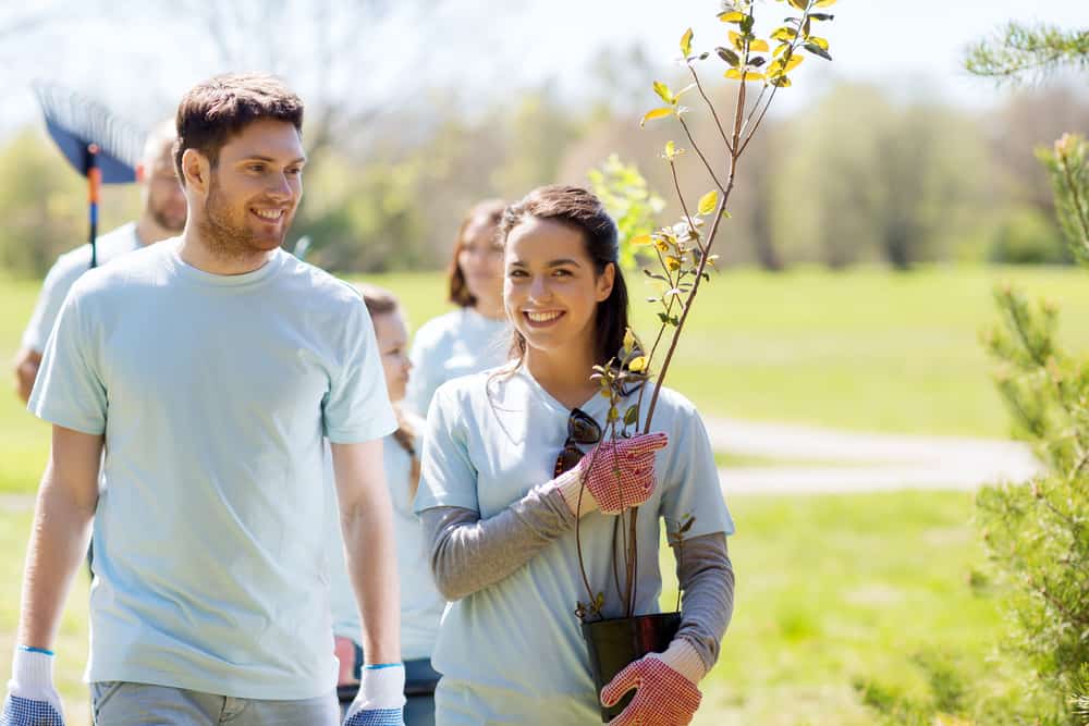 A group of volunteers stand with tree seedlings in the park.