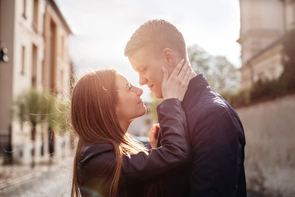 A young couple leans in to kiss one another outdoors.