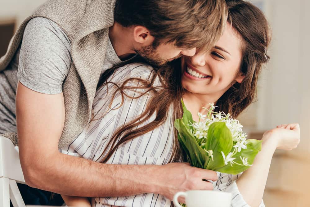 A man leans in to kiss a woman while handing her flowers.