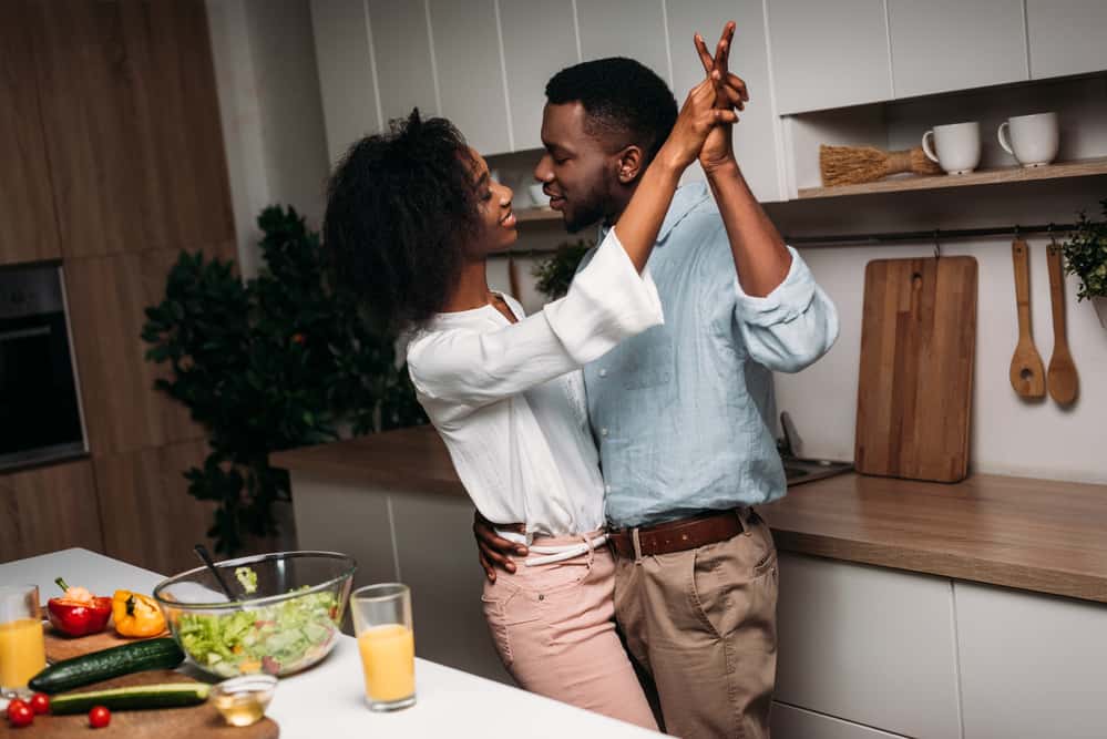 A couple dances in a kitchen with food sitting on the island next to them.
