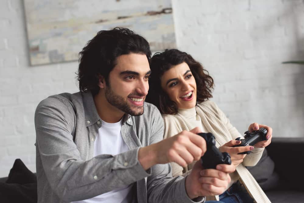A man and woman laugh while playing a game and holding controllers.