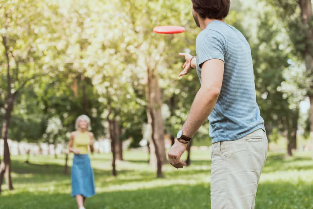 A man throws a frisbee to a woman in the forest.