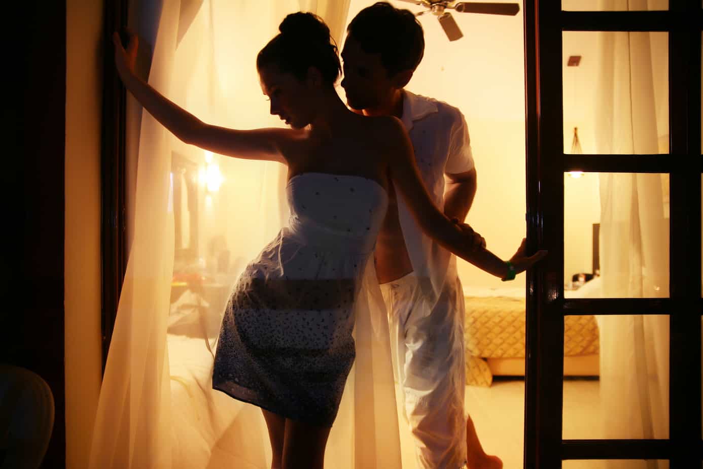 A couple is silhouetted against golden light while standing on a hotel balcony.