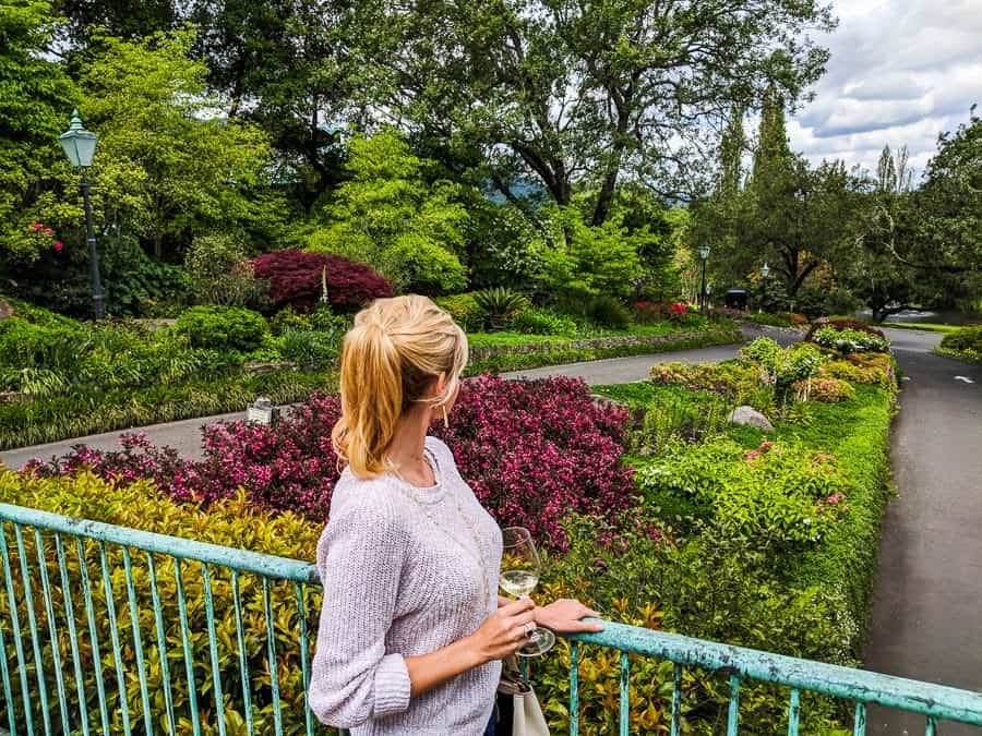 A woman holds a glass of wine while looking out to a garden.