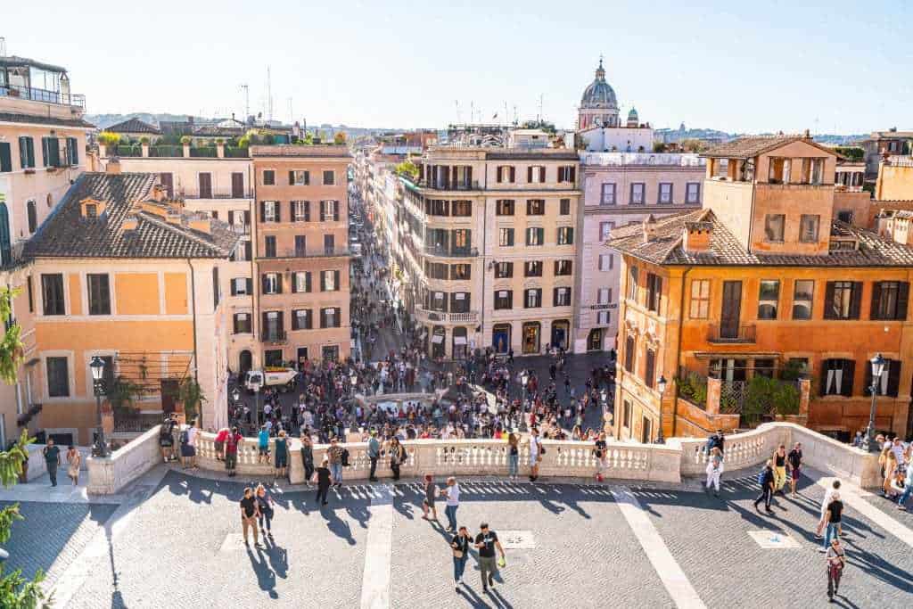 Crowds of people walking around a viewpoint looking out over a European city. 