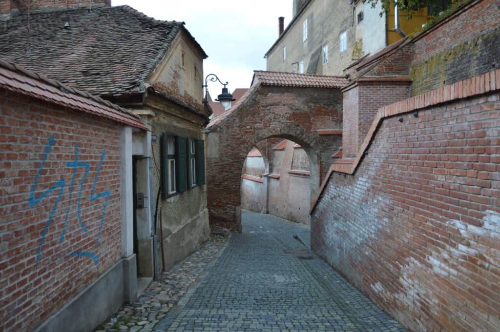 A small brick road with an arch over the center of it and brick buildings on either side of it. 