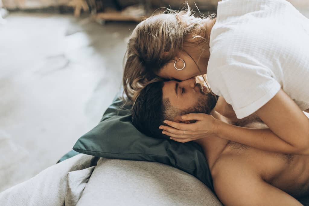 A woman kisses a man\'s forehead while laying in bed.