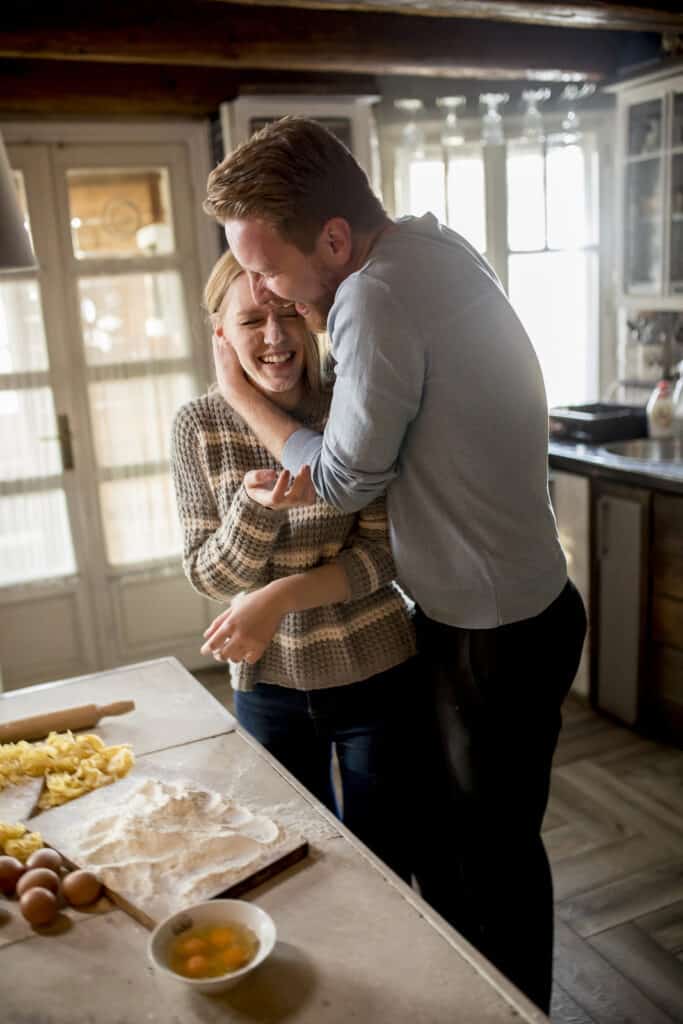 A couple embraces each other in a kitchen while baking together.