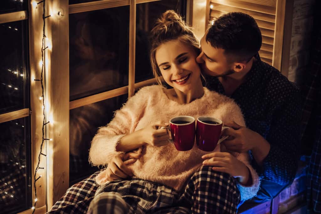 A man holds a woman while they both hold red mugs.