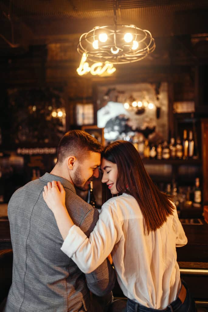 A couple sits in a bar forehead to forehead while smiling.